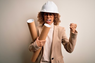 African american curly architect woman wearing safety helmet and glasses holding blueprints annoyed and frustrated shouting with anger, crazy and yelling with raised hand, anger concept