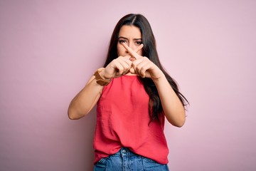 Young brunette woman wearing casual summer shirt over pink isolated background Rejection expression crossing fingers doing negative sign