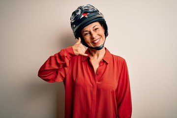 Middle age motorcyclist woman wearing motorcycle helmet over isolated white background smiling doing phone gesture with hand and fingers like talking on the telephone. Communicating concepts.