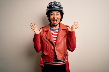 Middle age motorcyclist woman wearing motorcycle helmet and jacket over white background celebrating crazy and amazed for success with arms raised and open eyes screaming excited. Winner concept