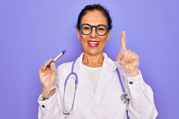 Middle age senior female doctor holding medice blood sample of coronavirus infection disease surprised with an idea or question pointing finger with happy face, number one