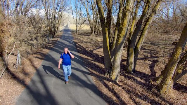 Older Man On A Nature Walk Can't Get Away From His Smartphone And Talks While Walking - Slow Motion Aerial View