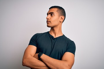 Young handsome african american man wearing casual t-shirt standing over white background looking to the side with arms crossed convinced and confident