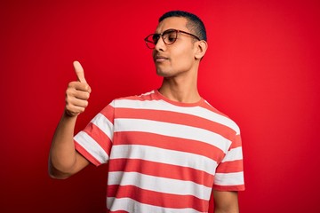 Naklejka premium Young handsome african american man wearing casual striped t-shirt and glasses Looking proud, smiling doing thumbs up gesture to the side