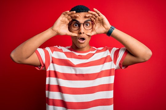 Young handsome african american man wearing casual striped t-shirt and glasses Trying to open eyes with fingers, sleepy and tired for morning fatigue