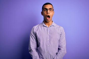 Handsome african american man wearing striped shirt and glasses over purple background afraid and shocked with surprise and amazed expression, fear and excited face.