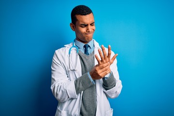 Handsome african american doctor man wearing coat and stethoscope over blue background Suffering pain on hands and fingers, arthritis inflammation