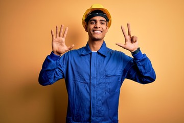 Young handsome african american worker man wearing blue uniform and security helmet showing and pointing up with fingers number eight while smiling confident and happy.