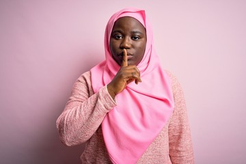 Young african american plus size woman wearing muslim hijab over isolated pink background asking to be quiet with finger on lips. Silence and secret concept.