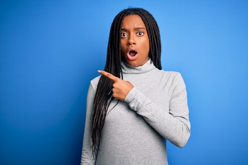 Young african american woman standing wearing casual turtleneck over blue isolated background Surprised pointing with finger to the side, open mouth amazed expression.