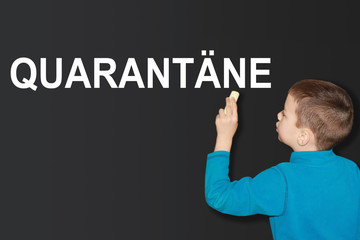a boy in a blue sweater writes on a black school blackboard with