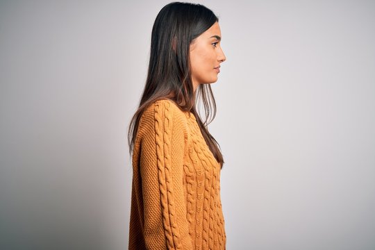 Young beautiful brunette woman wearing casual sweater over isolated white background looking to side, relax profile pose with natural face and confident smile.