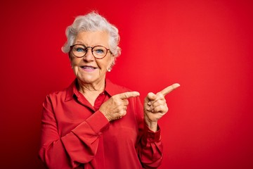 Senior beautiful grey-haired woman wearing casual shirt and glasses over red background smiling and...