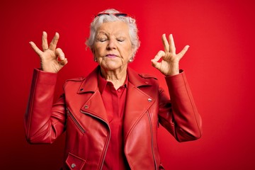 Senior beautiful grey-haired woman wearing casual red jacket and sunglasses relax and smiling with eyes closed doing meditation gesture with fingers. Yoga concept.