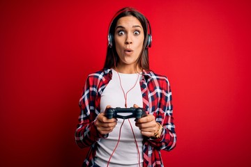 Young beautiful brunette gamer woman playing video game using joystick and headphones scared in...
