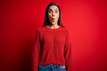 Beautiful young brunette woman wearing casual sweater standing over red isolated background afraid...