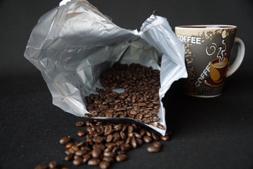Roasted coffee beans in a coffee bag beside the coffee cup
