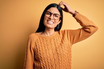 Young beautiful hispanic woman wearing glasses over yellow isolated background confuse and wonder...