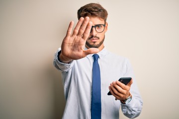 Young businessman having a conversation using smartphone over white background with open hand doing stop sign with serious and confident expression, defense gesture