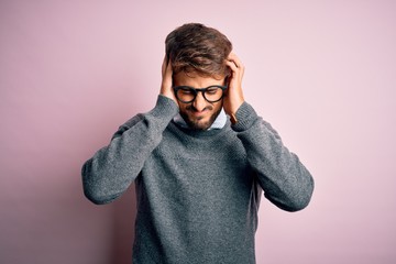 Young handsome man with beard wearing glasses and sweater standing over pink background suffering...