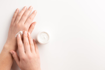 Care cosmetic concept. Woman applying cosmetic cream on hands, isolated on white background. Flat lay, top view, copy space.