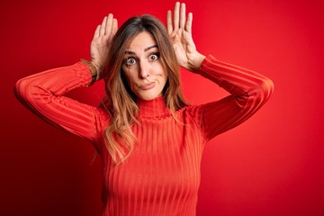 Obraz na płótnie Canvas Young beautiful brunette woman wearing casual turtleneck sweater over red background Doing bunny ears gesture with hands palms looking cynical and skeptical. Easter rabbit concept.