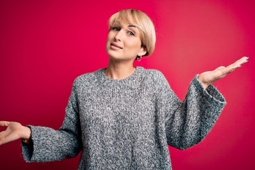 Young blonde woman with modern short hair wearing casual sweater over pink background clueless and...
