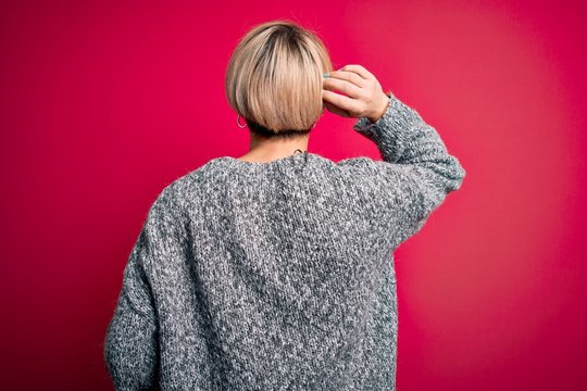 Young blonde woman with modern short hair wearing casual sweater over pink background Backwards thinking about doubt with hand on head