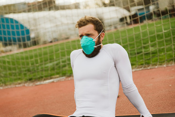 A muscular athlete in a white T-shirt wearing a medical protective mask trains outside during a coronavirus