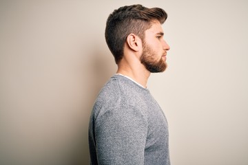 Young handsome blond man with beard and blue eyes wearing casual sweater looking to side, relax...