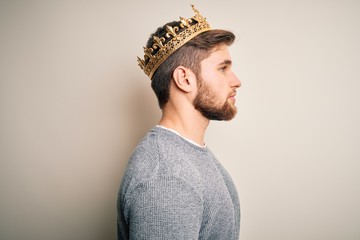 Young blond man with beard and blue eyes wearing golden crown of king looking to side, relax...