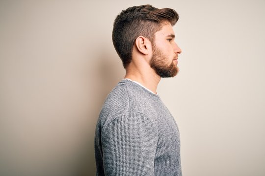 Young handsome blond man with beard and blue eyes wearing casual sweater looking to side, relax profile pose with natural face with confident smile.