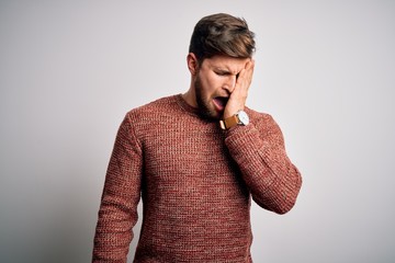 Young blond man with beard and blue eyes wearing casual sweater over white background Yawning tired covering half face, eye and mouth with hand. Face hurts in pain.