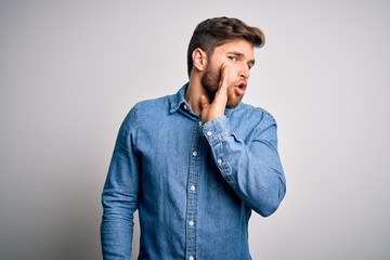Young handsome blond man with beard and blue eyes wearing casual denim shirt hand on mouth telling secret rumor, whispering malicious talk conversation