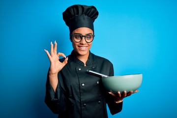 Young african american chef girl wearing cooker uniform and hat using whisk and bowl doing ok sign with fingers, excellent symbol