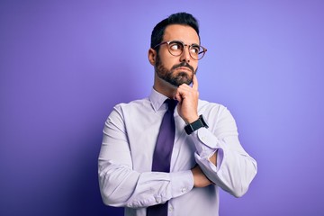 Handsome businessman with beard wearing casual tie and glasses over purple background with hand on chin thinking about question, pensive expression. Smiling with thoughtful face. Doubt concept.