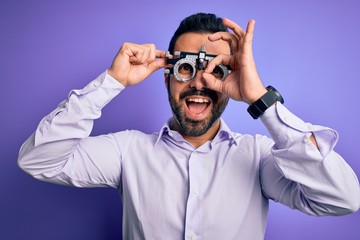 Young handsome optical man with beard wearing optometry glasses over purple background with happy face smiling doing ok sign with hand on eye looking through fingers
