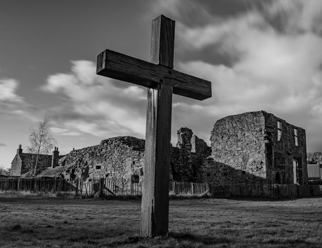 a religious cross with church ruin in background, storm clouds and meadow in black and white.