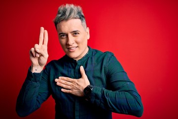 Young handsome modern man wearing elegant green shirt over red isolated background smiling swearing...