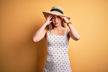 Young beautiful blonde woman on vacation wearing summer hat over yellow background suffering from headache desperate and stressed because pain and migraine. Hands on head.