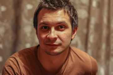 Fototapeta premium Portrait of a young seriously man at home on the background of the bookcase looking to camera.