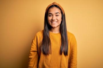 Young beautiful asian woman wearing casual sweater and diadem over yellow background with a happy and cool smile on face. Lucky person.