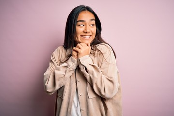 Young beautiful asian woman wearing casual shirt standing over pink background laughing nervous and excited with hands on chin looking to the side