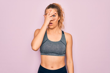 Young beautiful blonde sportswoman with blue eyes doing exercise wearing sportswear peeking in shock covering face and eyes with hand, looking through fingers with embarrassed expression.