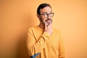 Obraz premium Middle age hoary man wearing casual sweater and glasses over isolated yellow background Thinking worried about a question, concerned and nervous with hand on chin