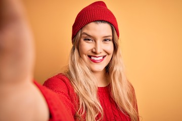 Young beautiful blonde woman making selfie by camera over isolated yellow background with a happy face standing and smiling with a confident smile showing teeth