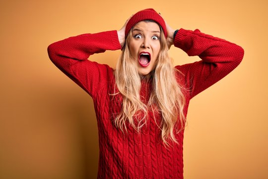 Young beautiful blonde woman wearing casual sweater and wool cap over white background Crazy and scared with hands on head, afraid and surprised of shock with open mouth