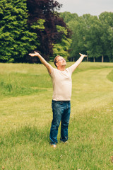 Happy middle age man enjoying nice day in summer park, holding arms up wide open