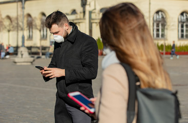 Woman and man are in masks with mobile phones on city street