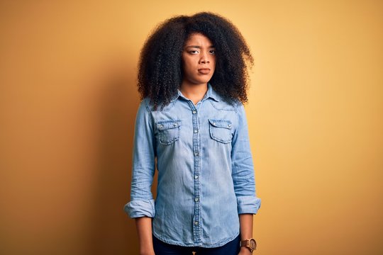 Young beautiful african american woman with afro hair standing over yellow isolated background skeptic and nervous, frowning upset because of problem. Negative person.